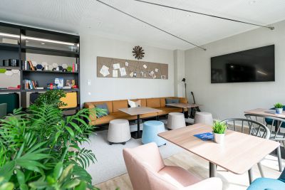 Farbenfreudiger Gemeinschaftsraum mit gemütlichem Sofa und Hockern in Kombination mit Tischen und Sesseln