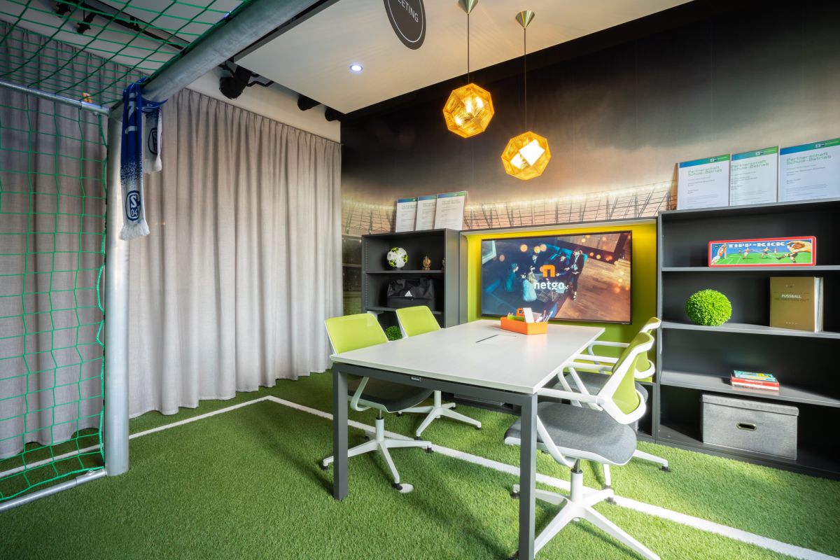 Meetingraum mit einem vierer Teamarbeitsplatz gestaltet wie ein Fußballsplatz mit einem Tor im Vordergrund und einem Kunstrasenteppich mit Fußballfeldmarkierungen